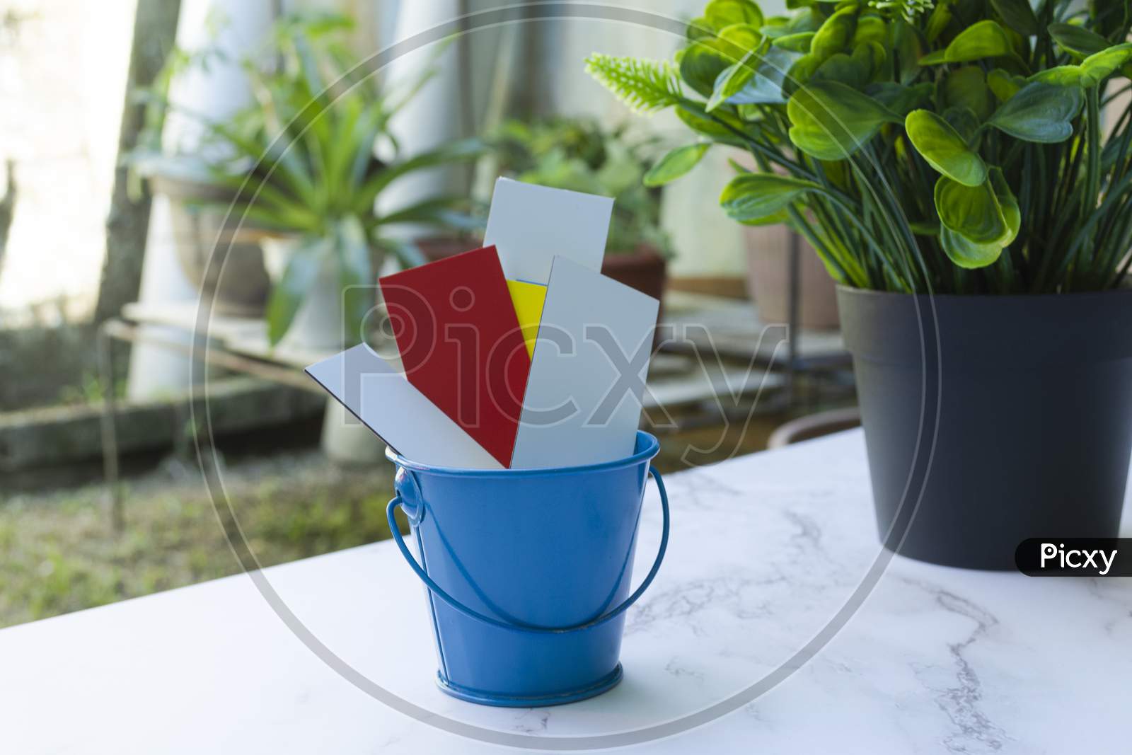 Colorful Paper Inside Of A Blue Bucket With Garden Background
