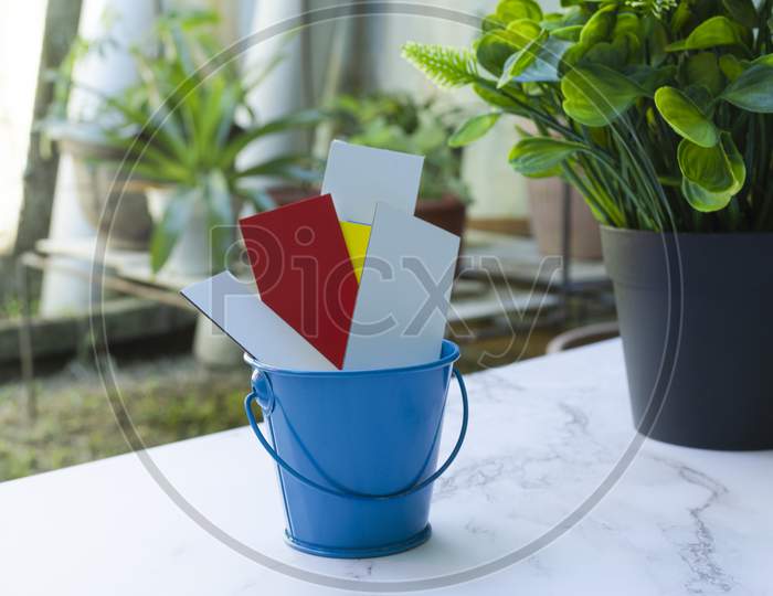 Colorful Paper Inside Of A Blue Bucket With Garden Background