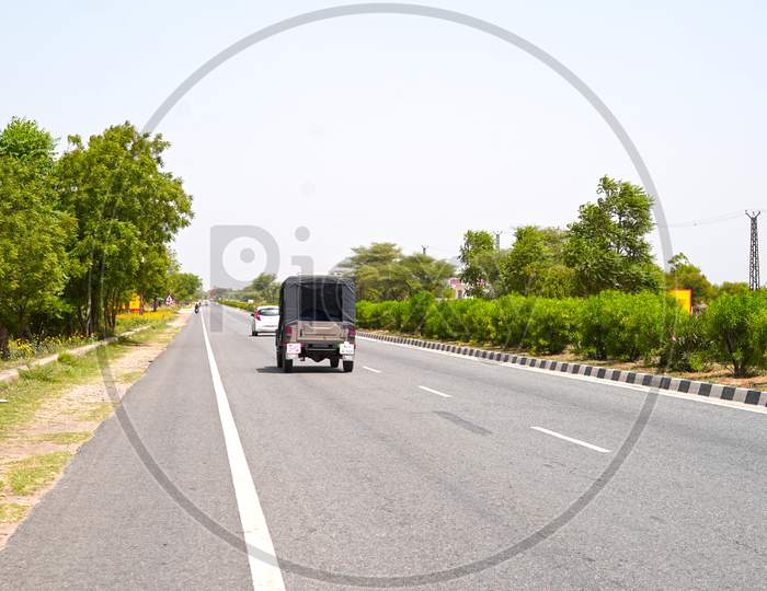 Long Asphalt Highway Road And Vehicles Passing Through Forest. Asphalt Road Transportation Road With Green Boulevard Path.