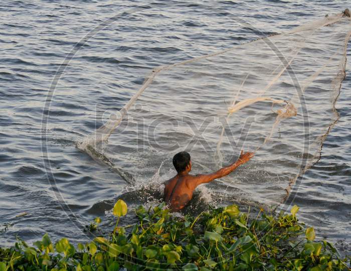 A shirtless fisherman throwing fishing net into river to catch fish in Bangladesh