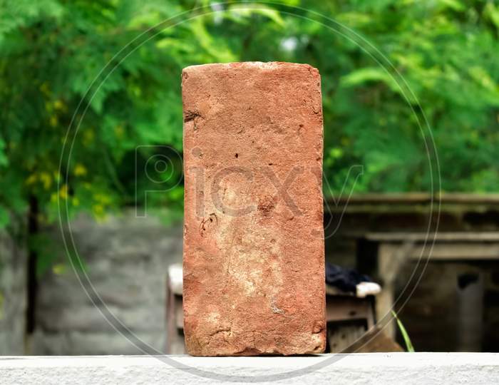 A Single Old Red Brick With Nice Blurry Green Background