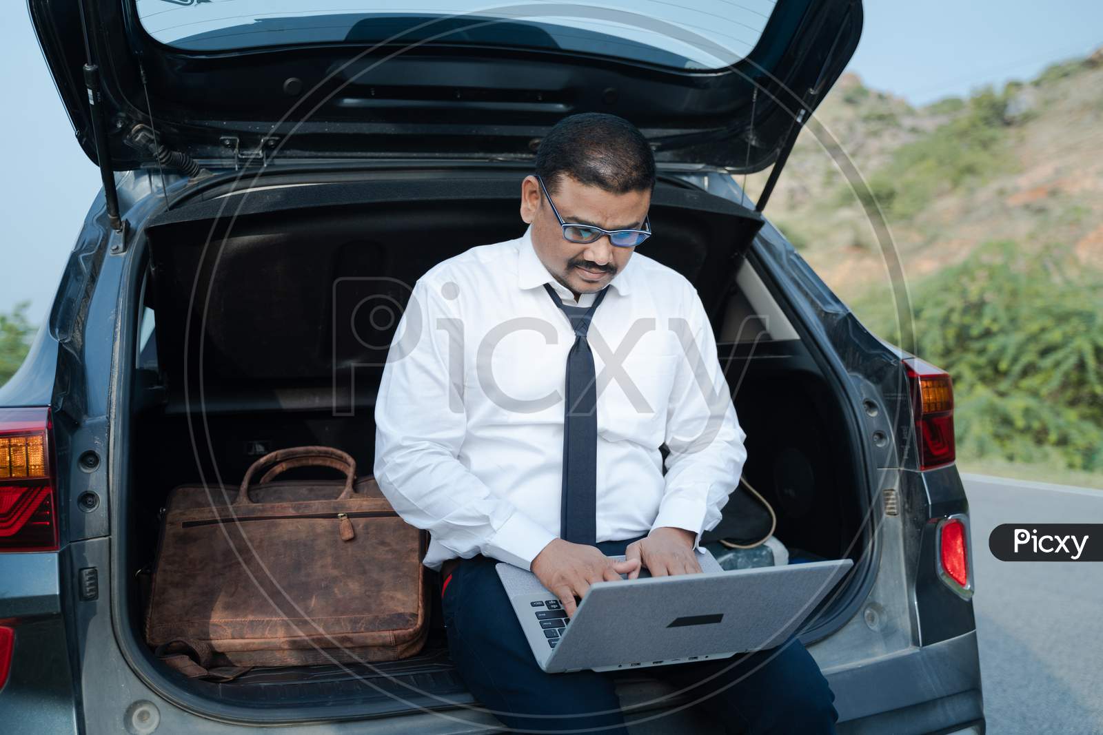Young Businessman Working From The Car Trunk Or Boot Near Roadside - Concept Of Digital Nomadic Lifestyle, Travel Freelancer And Vacations.
