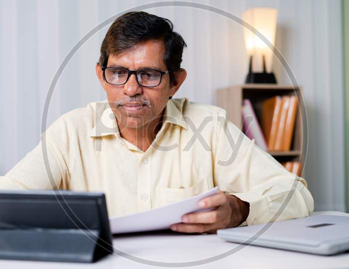 Businessman Checking Tax Or Contract Papers And Noting Down From Internet Using Tablet At Office - Concept Of Paper Work, E-Learning And Modern Working Using Technology.