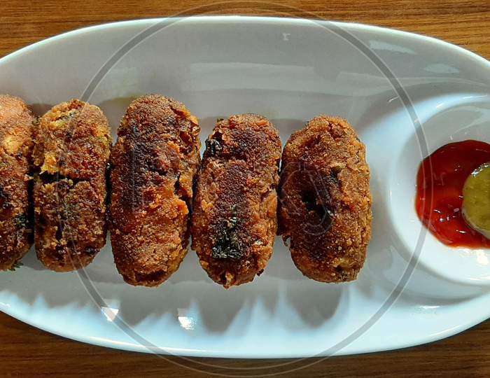 Veg cutlet with tomato and chilli chutney, wooden background, white plate
