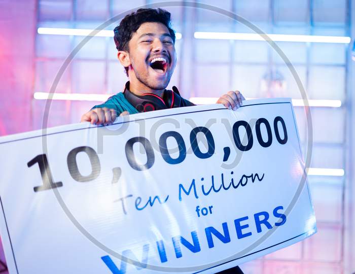 Excited Professional Esports Gamer With Headphones Celebrating And Dancing By Holding Winners Price Money Presentation At Video Gaming Tournament On Stage For Victory.