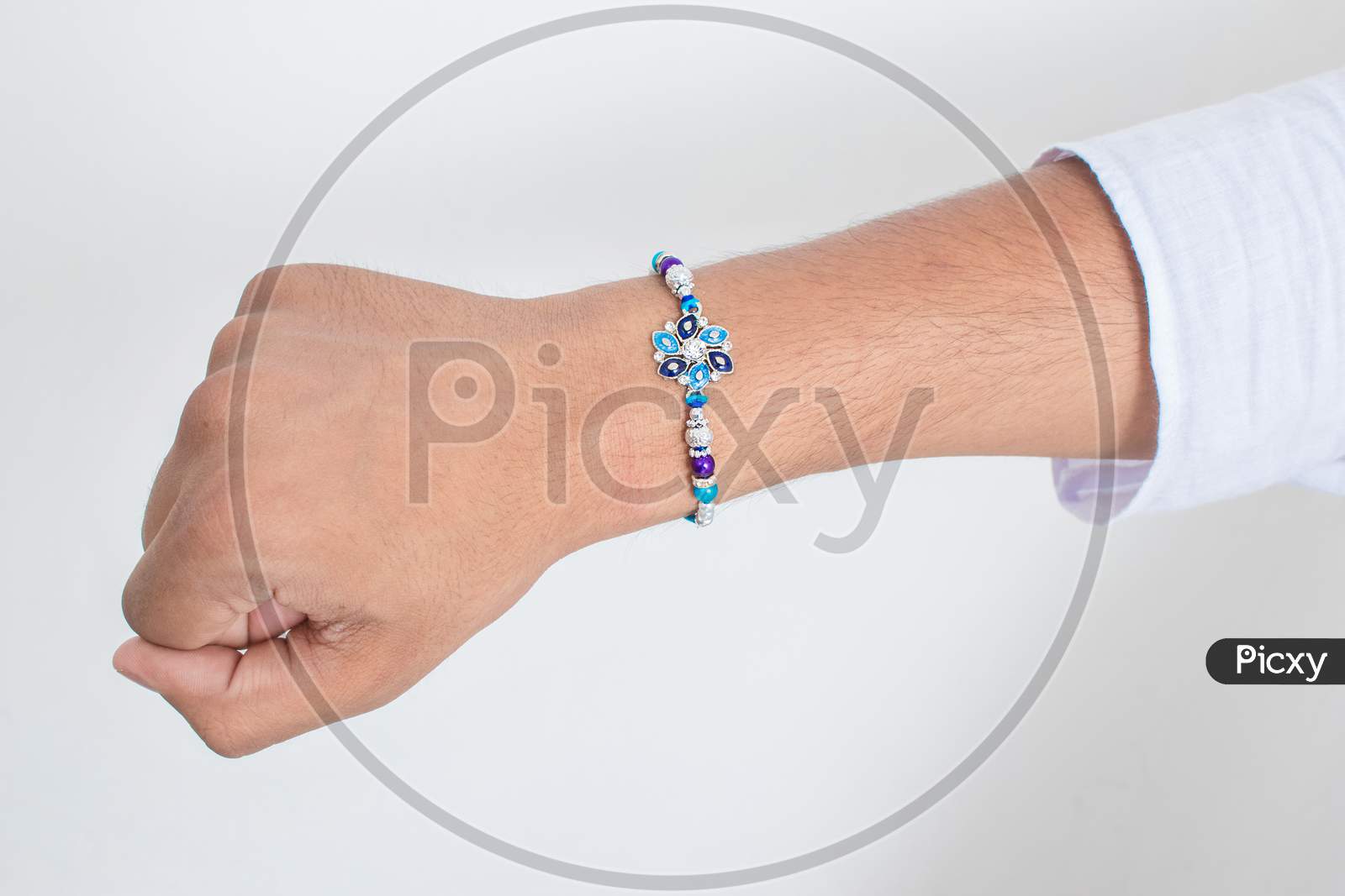 Hand Wearing Beautiful Blue Diamond Design Rakhi On The Occasion Of Raksha Bandhan Over White Background. Indian Festival Celebrated In India To Express Love And Bond Between Brother And Sister.