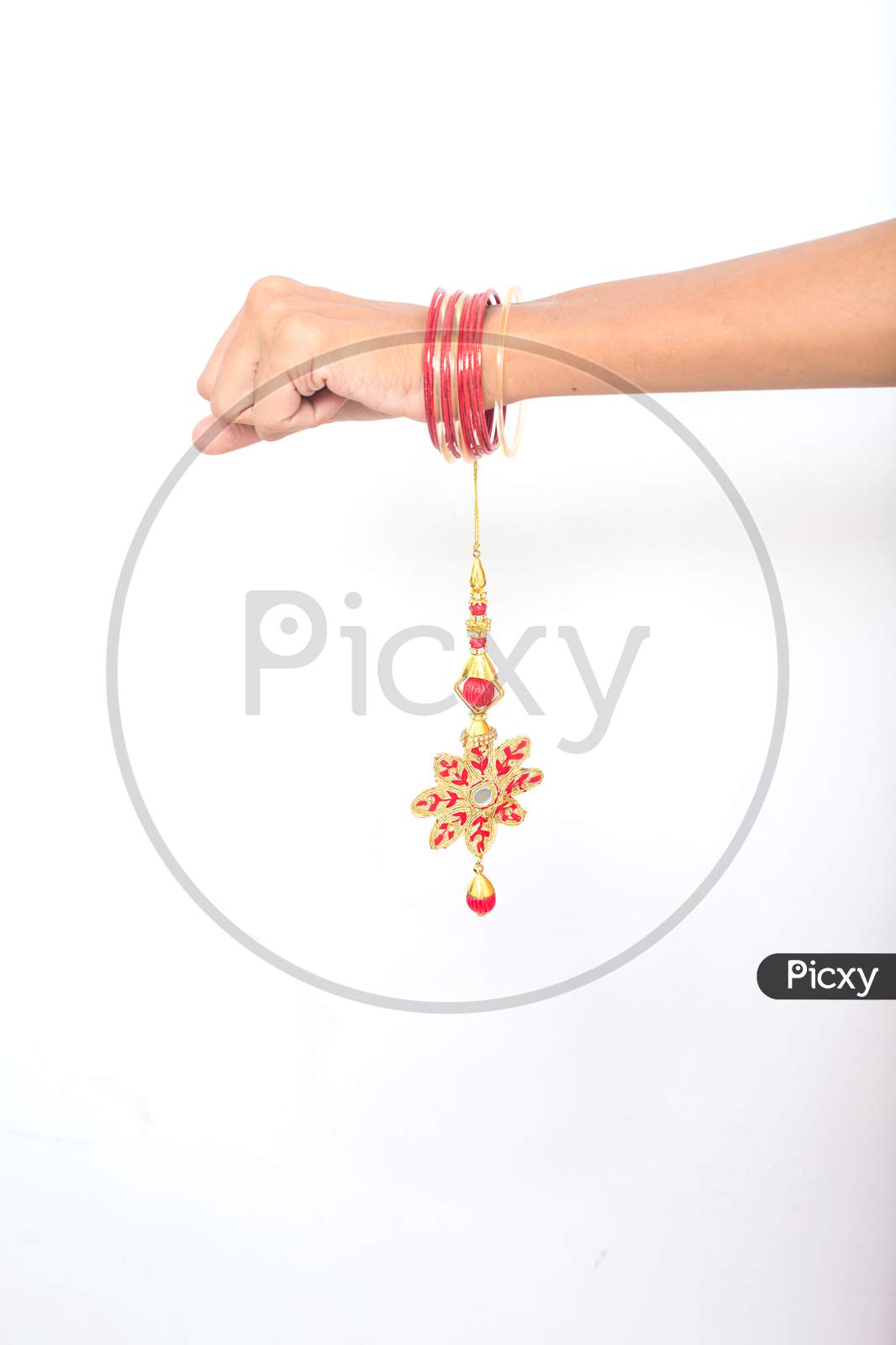 Female Hand Wearing Beautiful Red Lumba Rakhi On The Occasion Of Raksha Bandhan Over White Background. Silk Thread Floral Design Bracelet, Indian Festival Celebration.Copy Space.