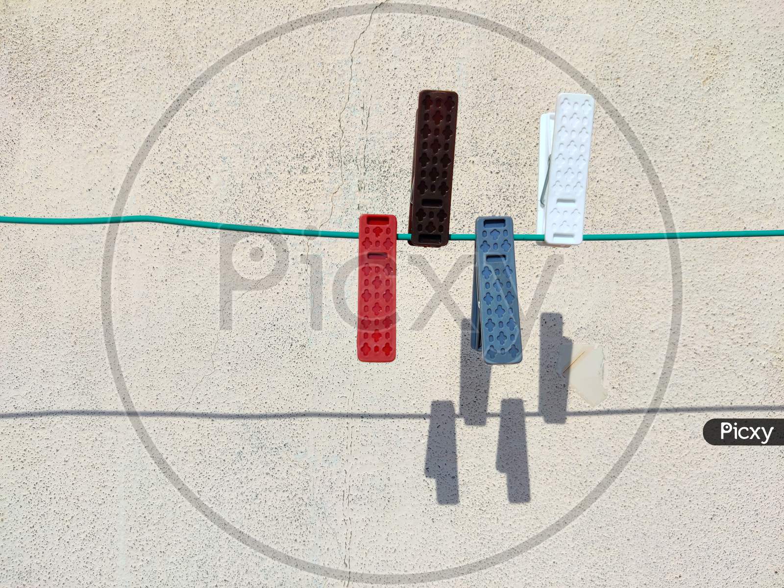 Four Colorful Cloth Clip Or Plastic Clothespins On The Rope With Shadows On White Background