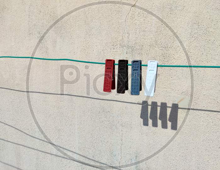 Side View Of Grey,Red,Brown And White Color Clothespins Or Cloth Clips On The Rope With Shadows In Back. White Background