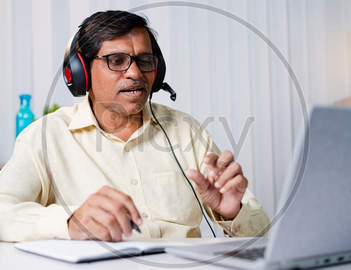 Middled Aged Businessman With Headphones Attending Online And Making Notes Glass From Office - Concept Of Never Stop Learning And Business Training