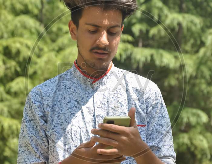 Portrait of a Indian handsome young guy standing outside with using mobile phone
