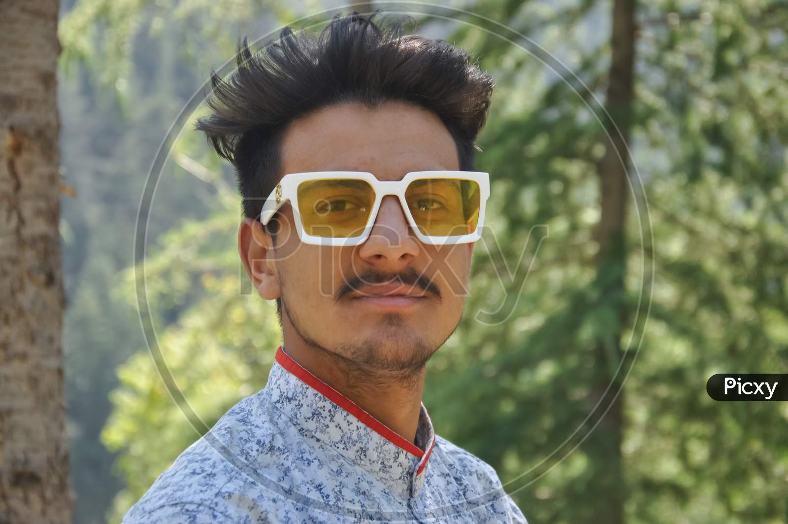Closeup of a good looking young guy standing outdoor in the nature and wearing sunglasses with looking at camera