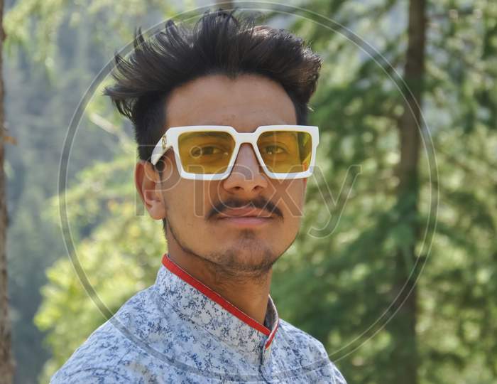 Closeup of a good looking young guy standing outdoor in the nature and wearing sunglasses with looking at camera