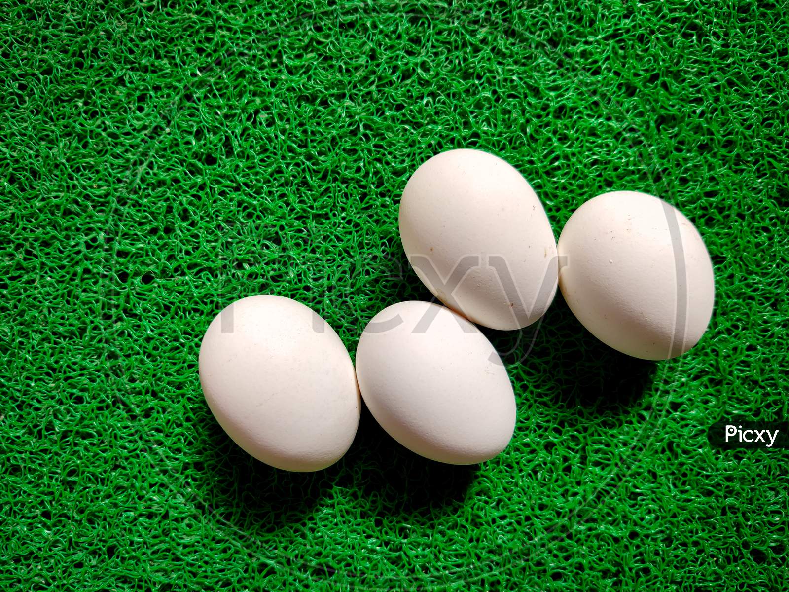 Four Raw White Eggs In Zigzag Manner Isolated On Green Background