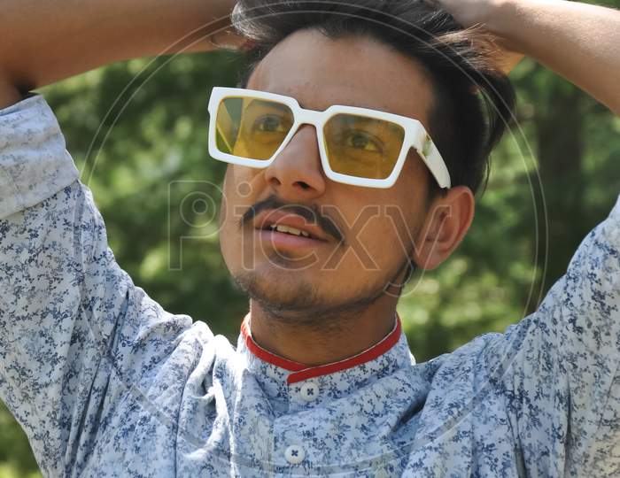 Portrait of a Indian handsome young guy wearing sunglasses posing outdoors with hands on hair with looking sideways