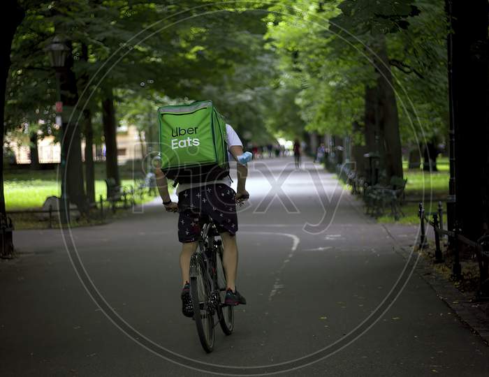 Krakow, Poland - August 01, 2021: A Delivery Man In A Bicycle Riding Through A Street In Order To Delivering Food In A Huge Bag Pack