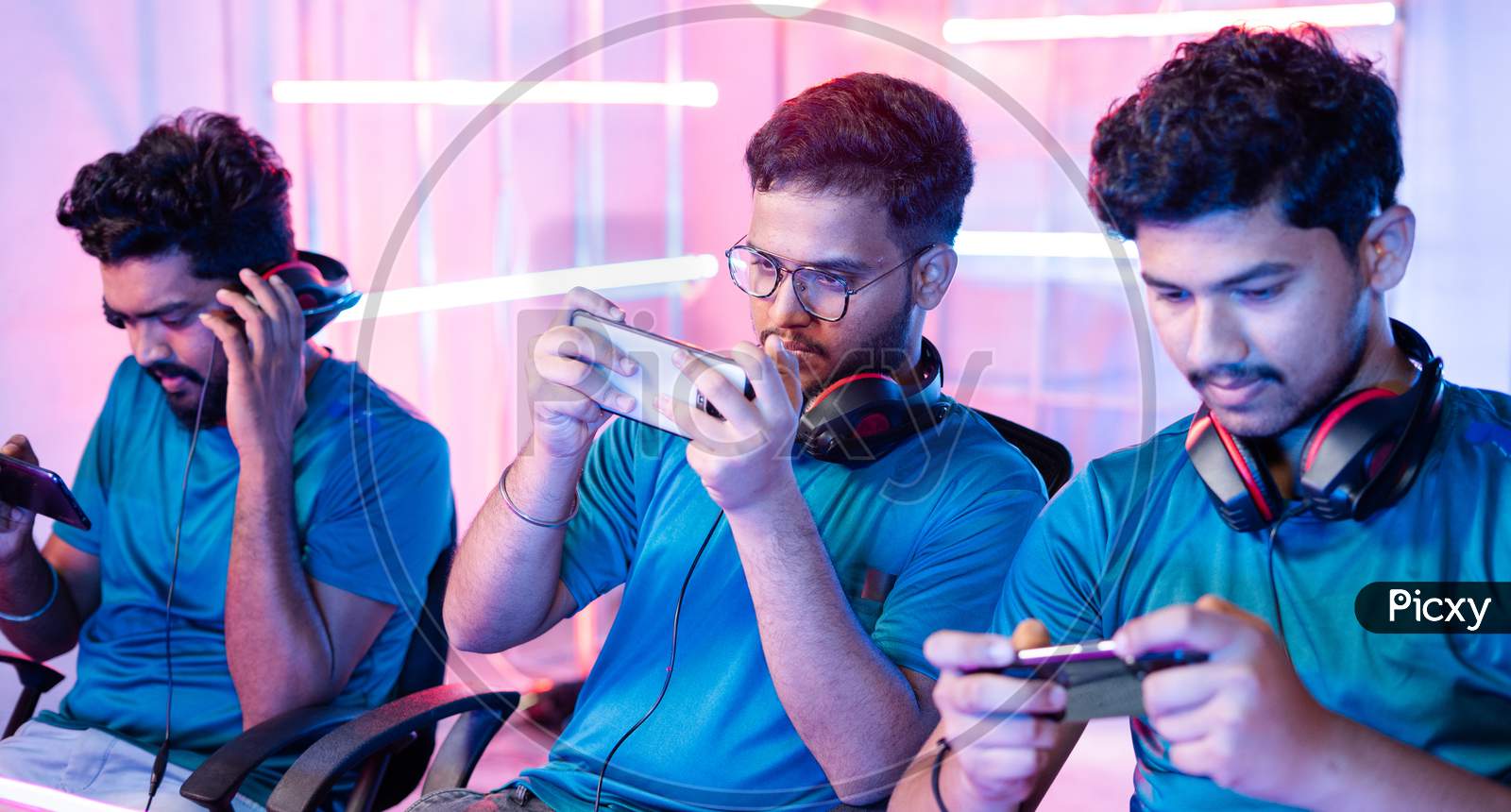 Team Of Young Professional Gamers Playing Live Video Game On Mobile Phone By Talking On Headphones At Esports League.