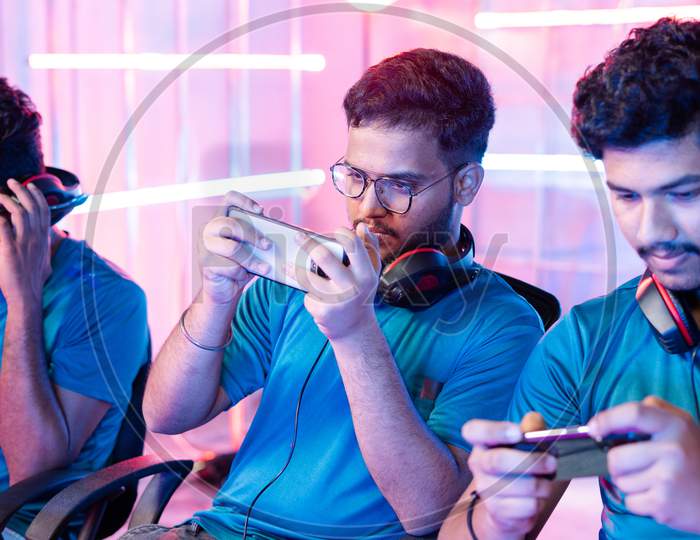 Team Of Young Professional Gamers Playing Live Video Game On Mobile Phone By Talking On Headphones At Esports League.