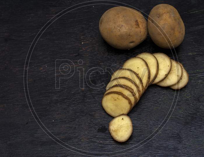 Two Whole Potatoes And A Sliced Potato On A Dark Background With Selective Focus
