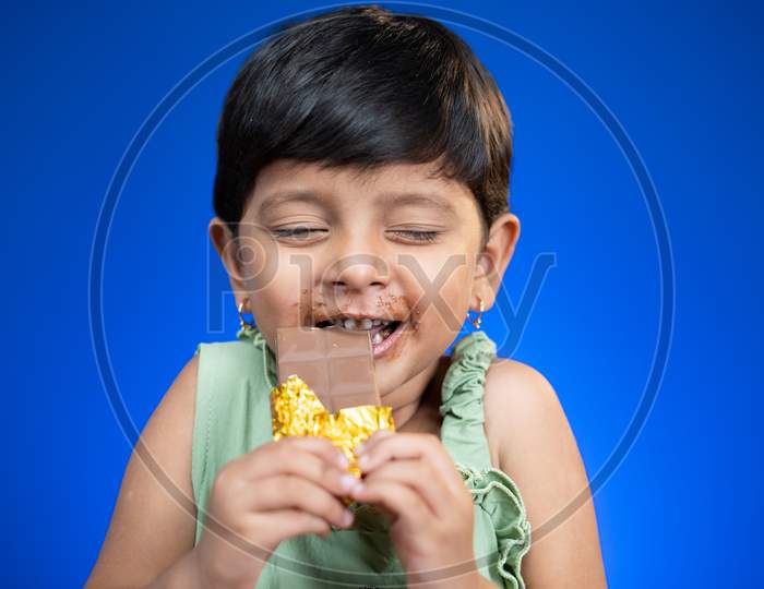 Happy Girl Kid Enjoying Chocolate Bite By Closing Eyes On Blue Background - Concepts Of Children'S Love And Addictions On Chocolates