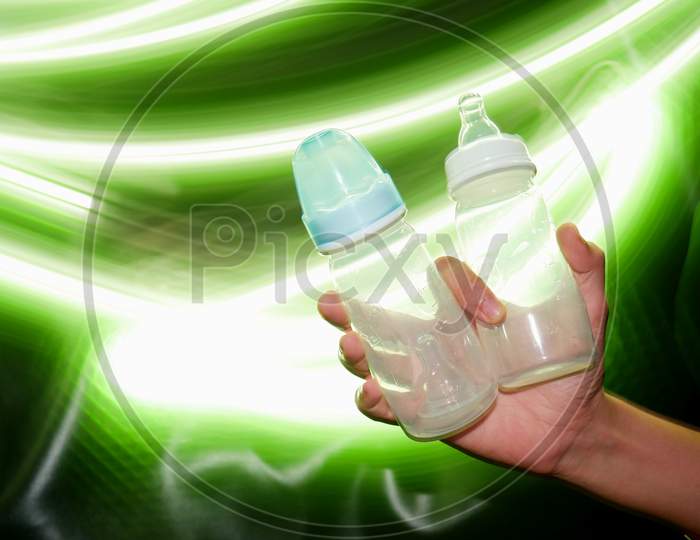 Baby Milk Feeding Nipple Bottles Presented On Female Hand With Light Effect Shine Backdrop, Commercial Product Presentation Image.