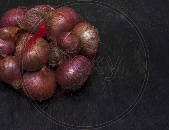 A Net Bag Full Of Onions On A Black Background With Selective Focus.