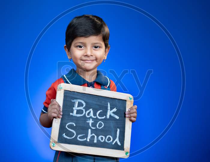 Happy Smiling Indian School Kid Holding Back To School Sign Board On Blue Background