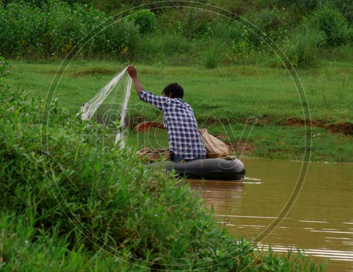Asian Village Fisher Man Catching Fishes From Filter Net At Lake Side.