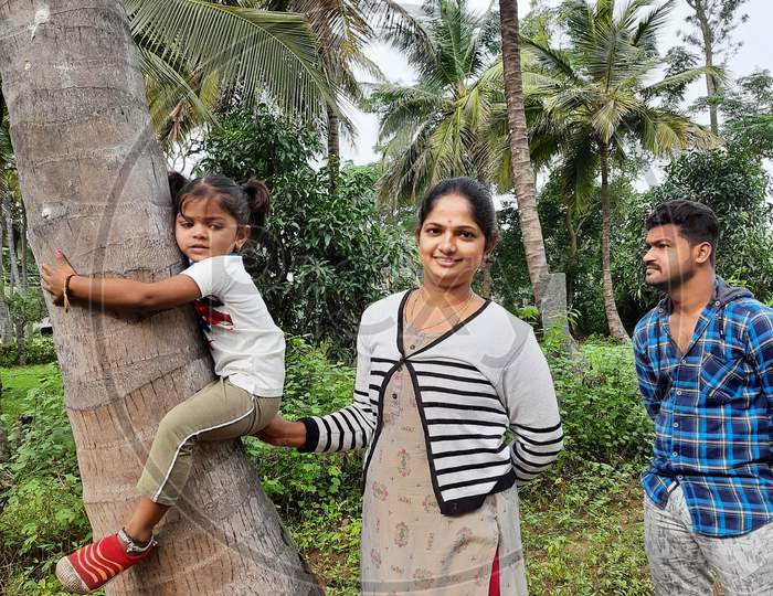 Closeup of Indian Mother and Father helping young Indian Kid to climbing a coconut tree in the farm