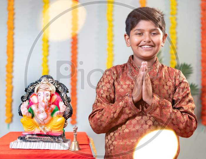 Happy Smiling Kid During Ganesha Festival With Traditional Dress Doing Namaste On Decorated Background