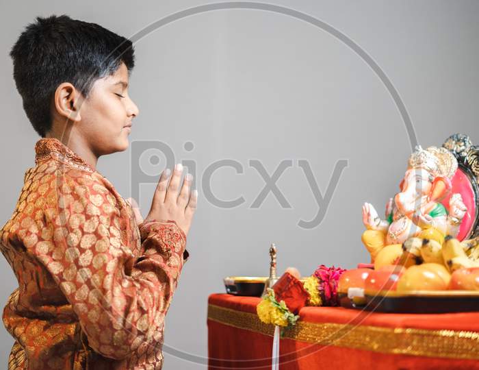 Studio Shot Of Kid During Ganesha Festival With Traditional Dress Praying In Front Of Idol Ganapati On Gray Background.