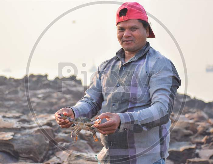 Fisherman Holding Giant Crab In His Hand At Sea Shore With Smile On His Face