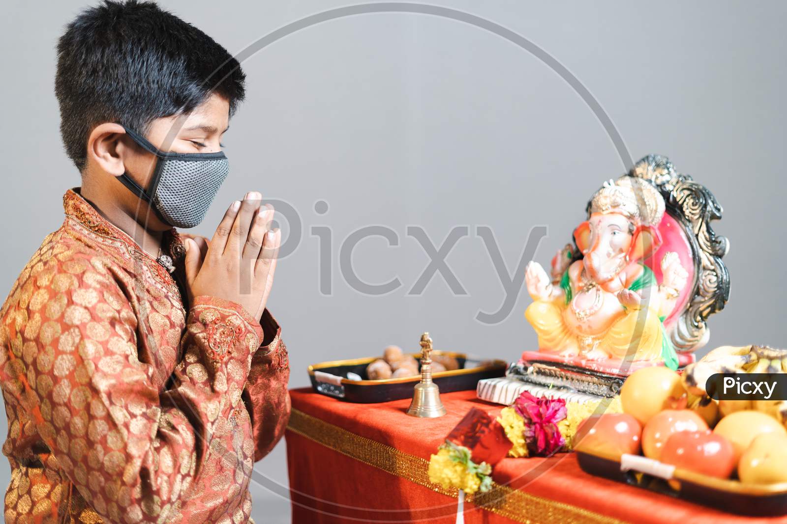Kid With Medical Face Mask Praying In Front Of The Ganesha Idol During Festival Celebrations With Traditional Dress During Coronavirus Covid Pandemic