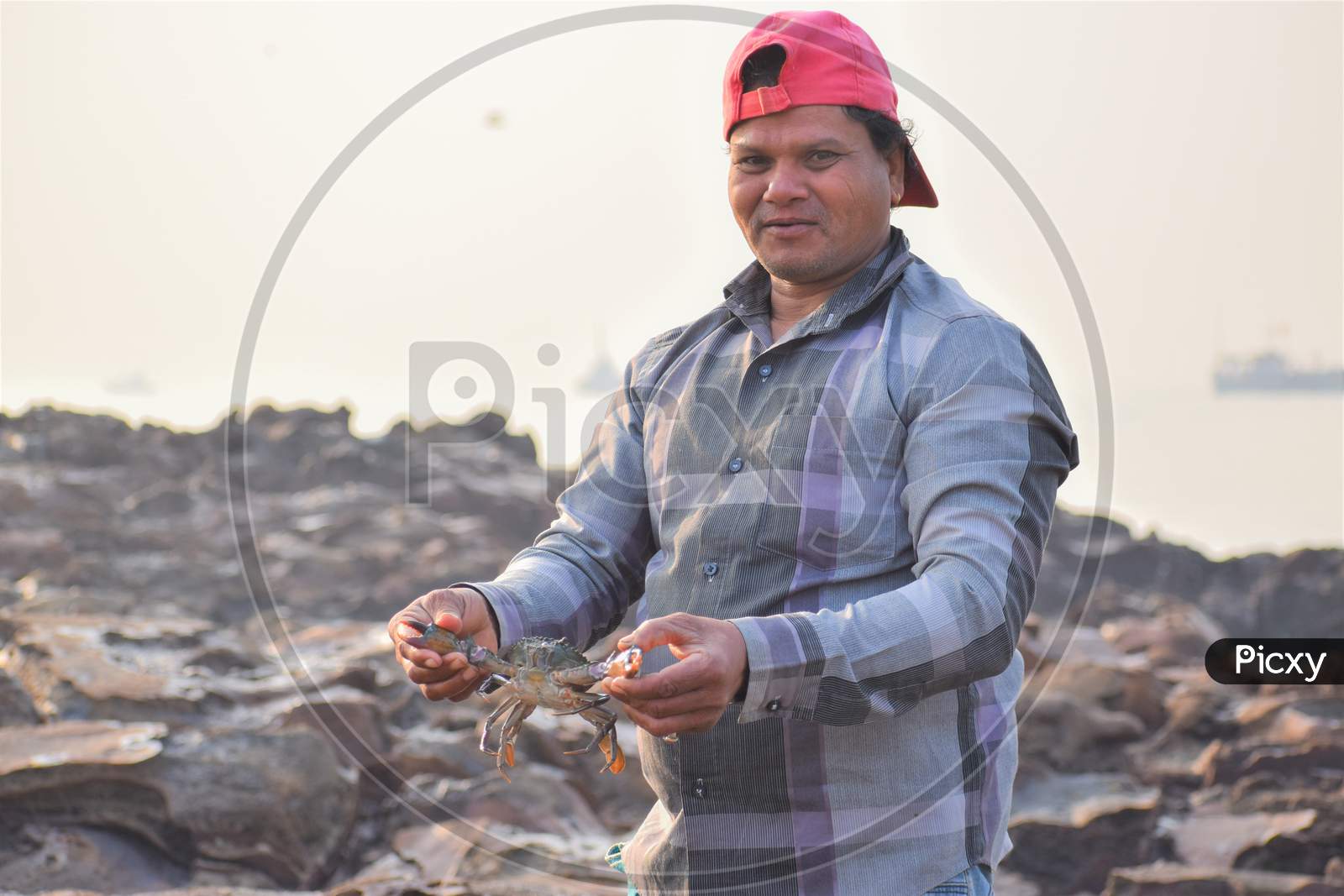 Fisherman Holding Giant Crab In His Hand At Sea Shore With Smile On His Face