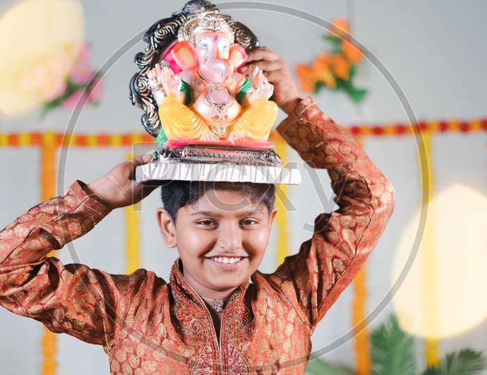 Happy Smiling Kid During Ganesha Festival With Traditional Dress Carrying Lord Vinayaka For Visarjan Or Immersion During Religious Celebration