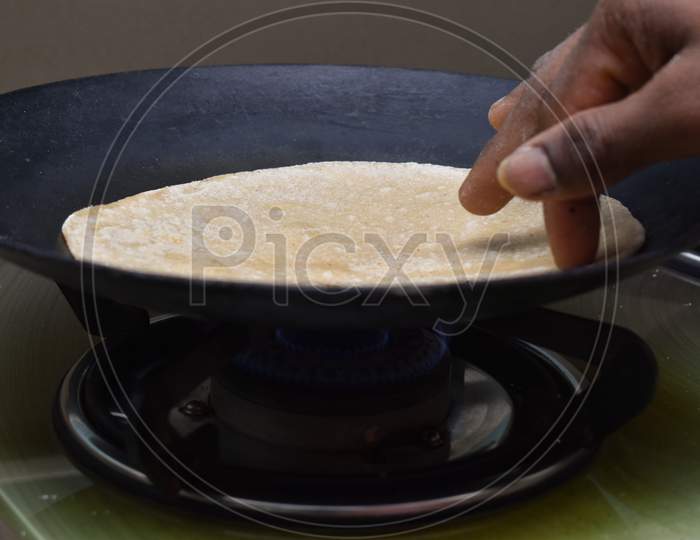 Making Roti (Indian Chapati) On Roti Tawa Made Of Wheat With Hand On Gas Stove