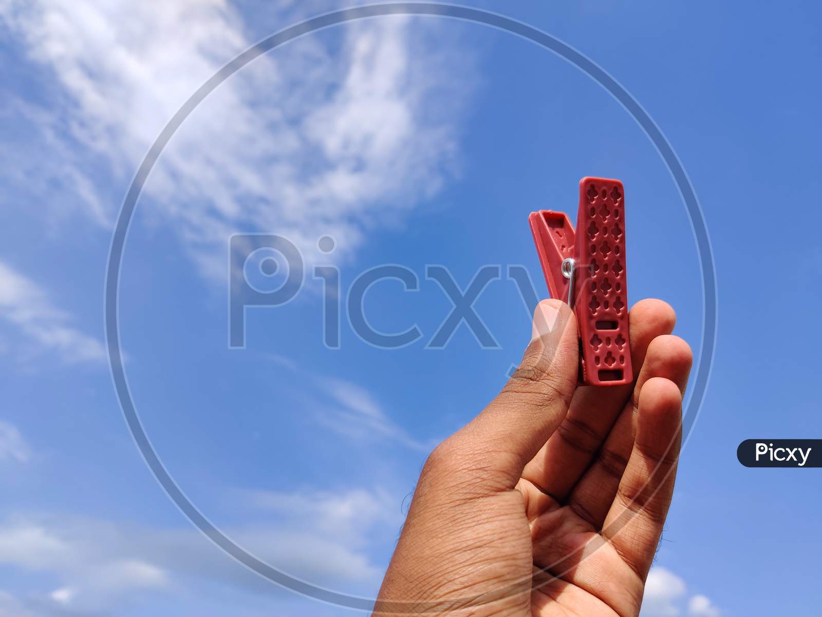 South Indian Young Man Holding Red Color Clothespin Or Cloth Clip.Cloud Background