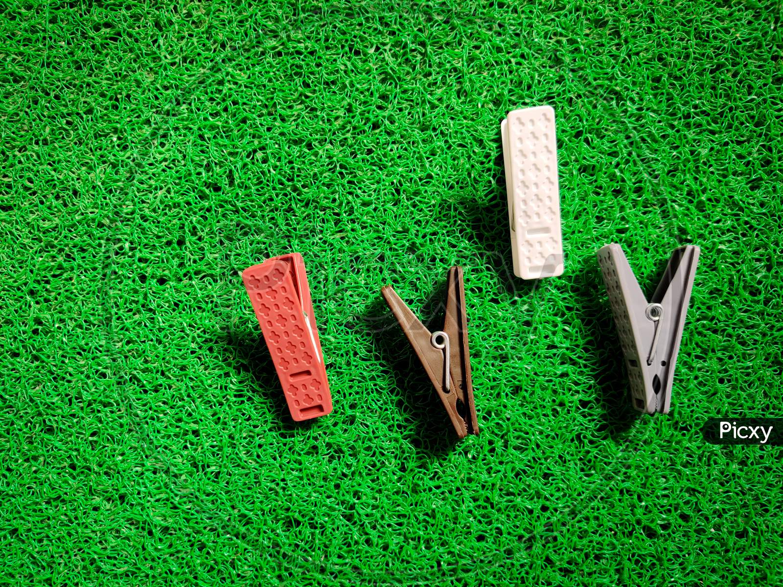 Four Different Colored Plastic Clothespins Or Clothesclips Isolated On Green Background