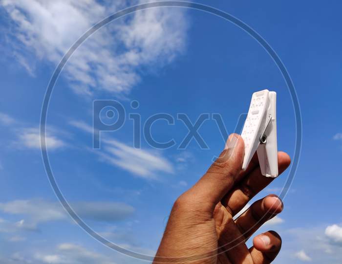 South Indian Young Man Holding White Color Clothespin Or Cloth Clip.Cloud Background