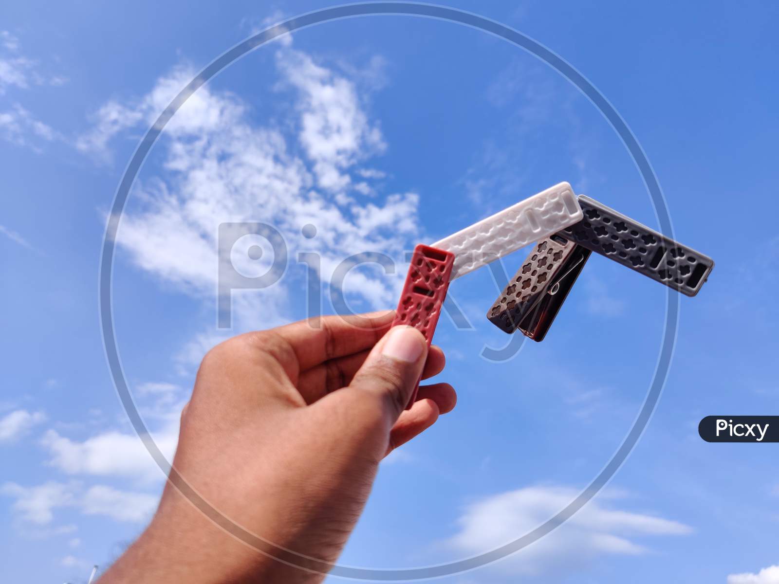 South Indian Young Man Holding Four Different Color Clothespin Or Cloth Clip.Cloud Background