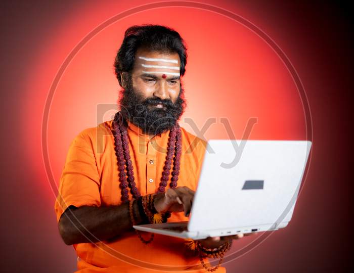 Holy Indian God Man Or Guru With Rudrakshi Mala Using Laptop - Concept Of Online Horoscope, Astrology And Fortune Telling Using Technology And Internet