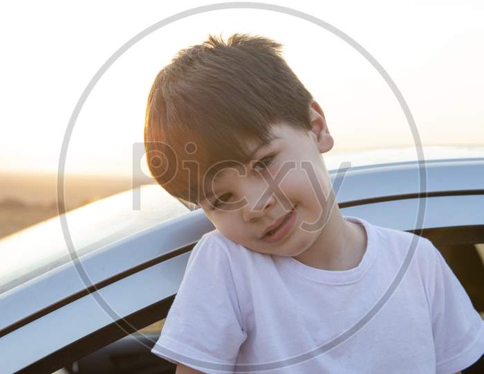 Closeup Of Charming Caucasian Boy With Shy Smile With His Body Out Of The Car