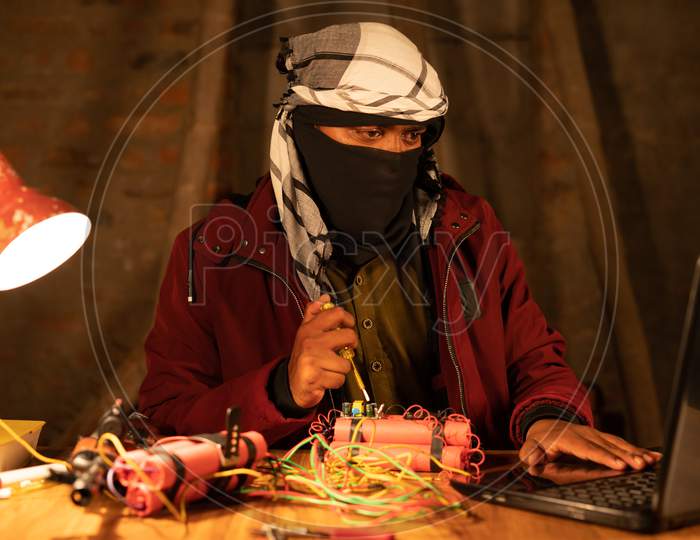 Militant With Face Cover Learning Timer Bomb Making With Dynamite By Looking Into Laptop.