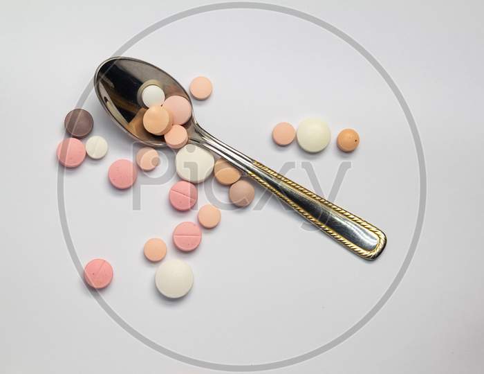 Colored Pills Or Medications On A Neutral Background Next To A Small Spoon.