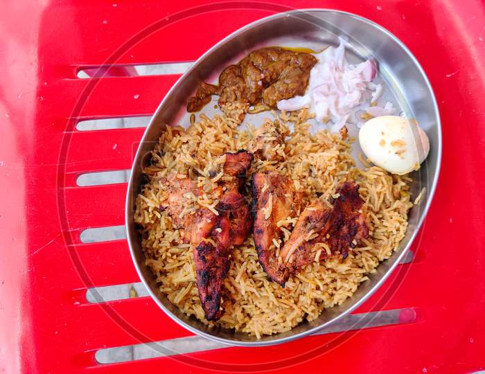 Top View Of Eating Plate Filled With Chicken Biryani, Two Tandoori Chicken, One Boiled Egg , Raitha And Brinjal Curry. A South Indian Basmathi Rice Sunday Lunch.