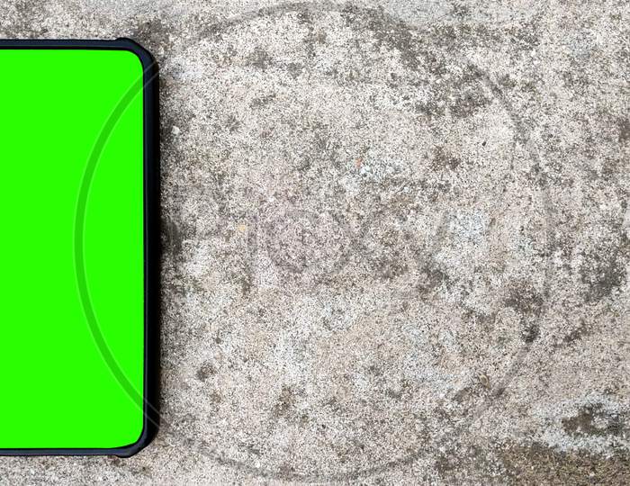 Top Angle Shot Of Black Smartphone With Green Screen On Concrete Background. Copy Space For Text