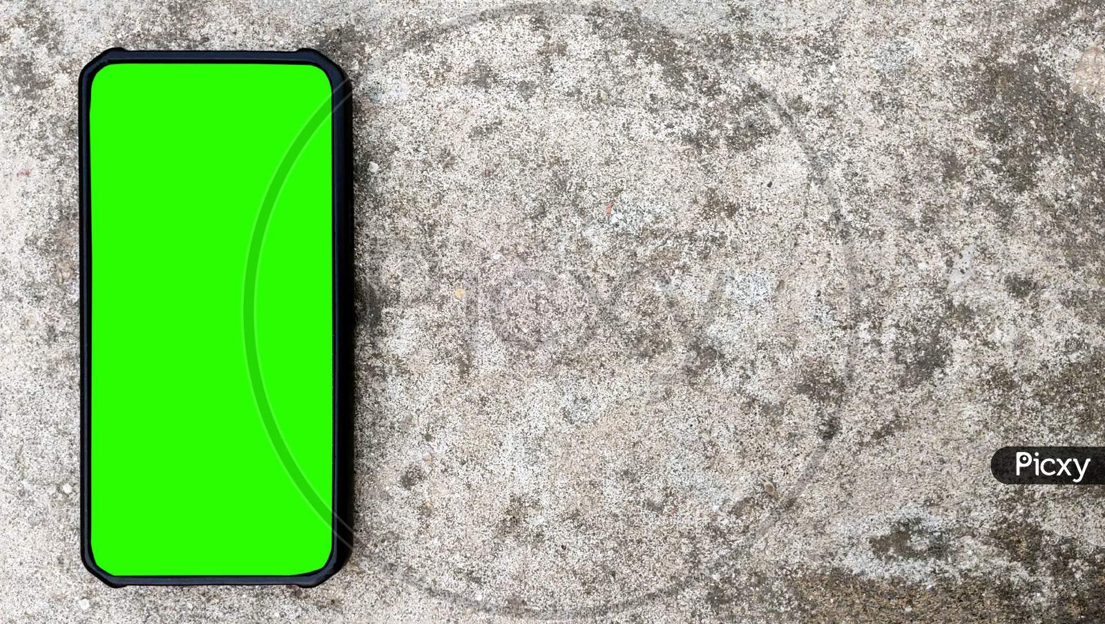 Top Angle Shot Of Black Smartphone With Green Screen On Concrete Background. Copy Space For Text