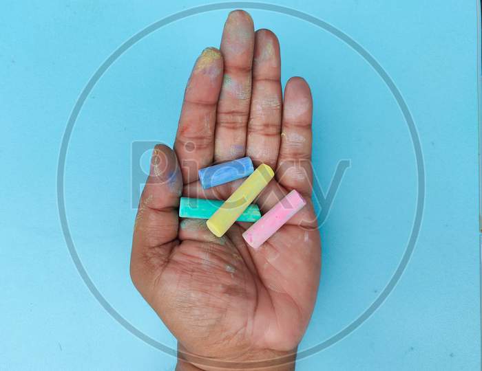 Top View Of Man''S Palm Full Of Colorful Chalks With Blue Back Ground.