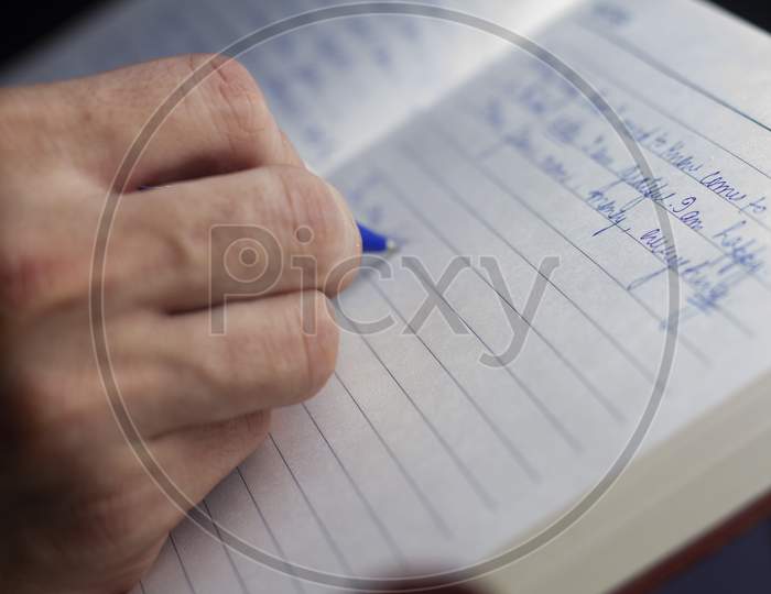 A Man Is Writing With A Blue Pen On A Notebook.Selective Focus