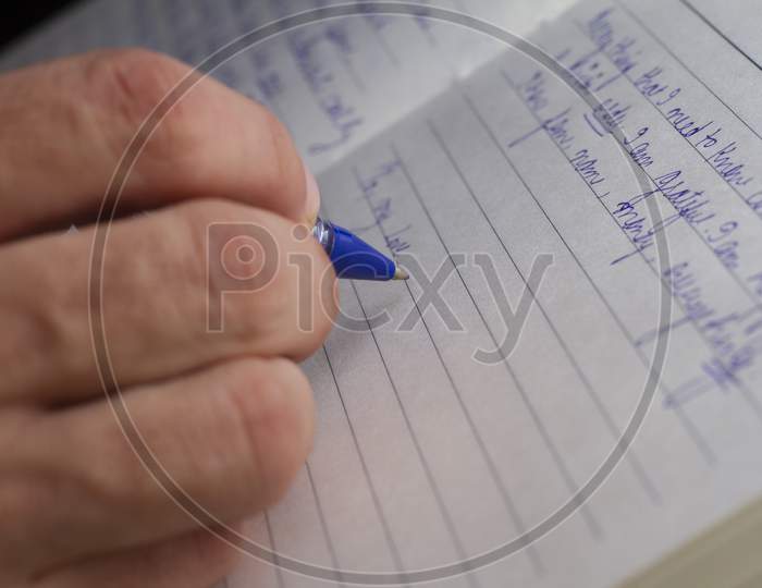 A Man Is Writing With A Blue Pen On A Notebook.Selective Focus